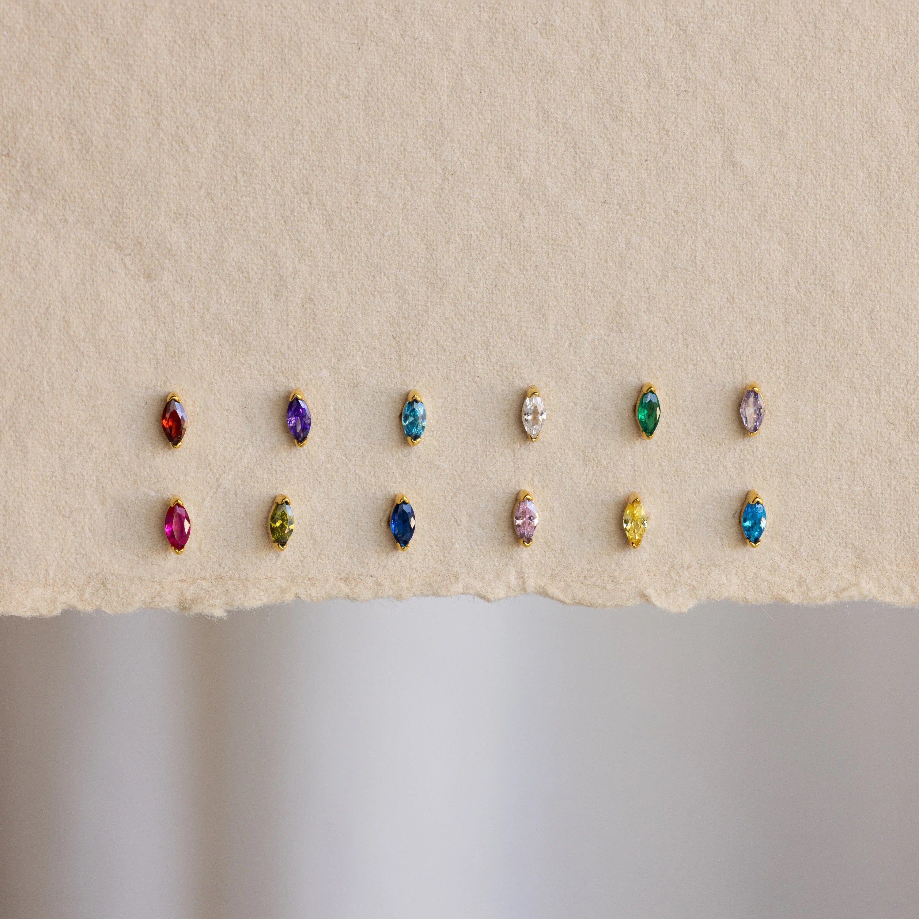 Row of multicolored gemstone earrings on a beige background